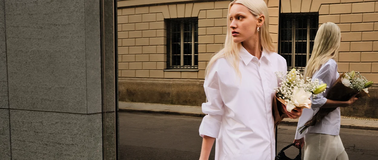 Woman holding a bouquet walks along a mirrored wall where her reflection is visible. (photo)