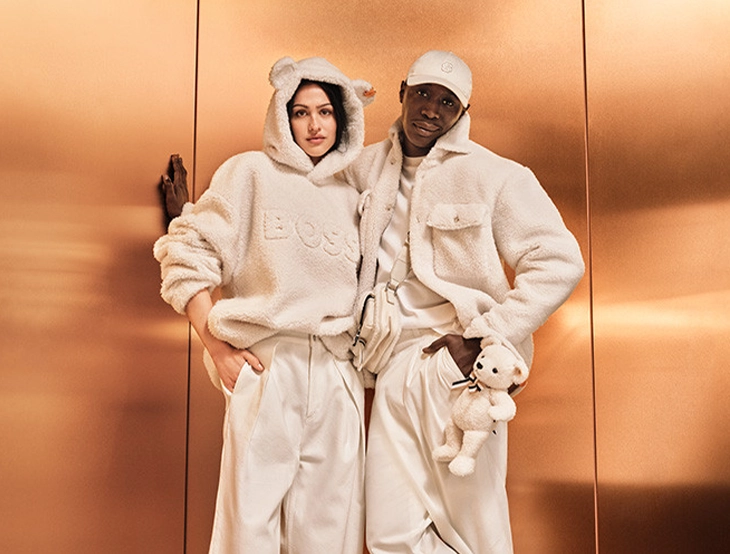 BOSS x Steiff holiday campaign – Khaby Lame and Amelia Gray pose in front of a copper-colored wall (photo).
